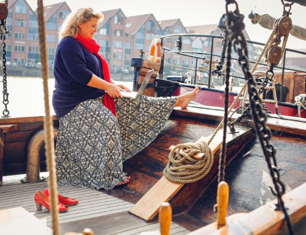 Birgit Gosejacob sitting on deck of a sailing boat in the harbour, writing on her laptop